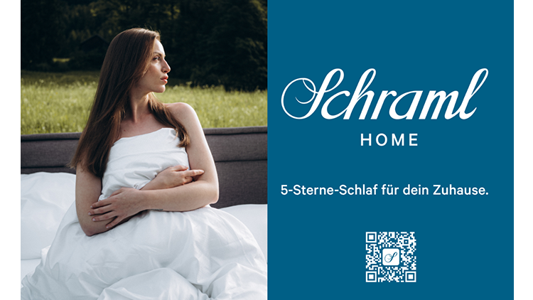 Advertisement for Schraml Home: a woman in a white duvet sits on a bed on the left; a blue panel on the right shows the Schraml logo and the phrase '5-Sterne-Schlaf für dein Zuhause', plus a QR code.